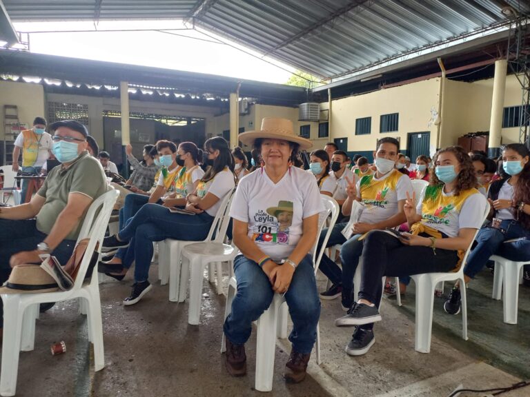 Grupo de personas y una sentada de frente con sombrero y camiseta blanca